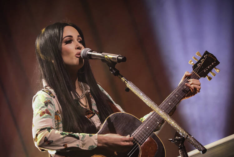 Photo of Kacey Musgraves singing and playing guitar at a concert